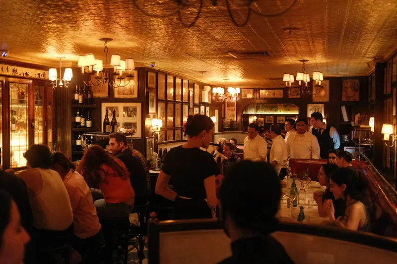 Gäste und Servicepersonal in einem belebten Restaurant mit warmem Licht (Symbolbild).